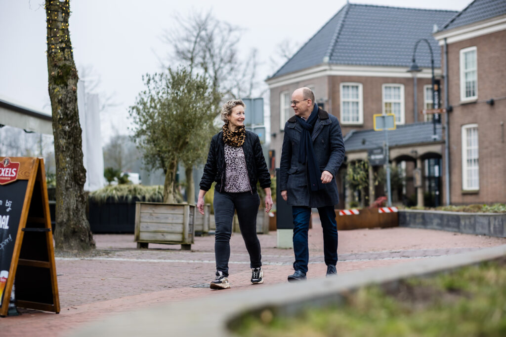 Man en vrouw wandelen samen over een klinkerplein langs een terrasbord